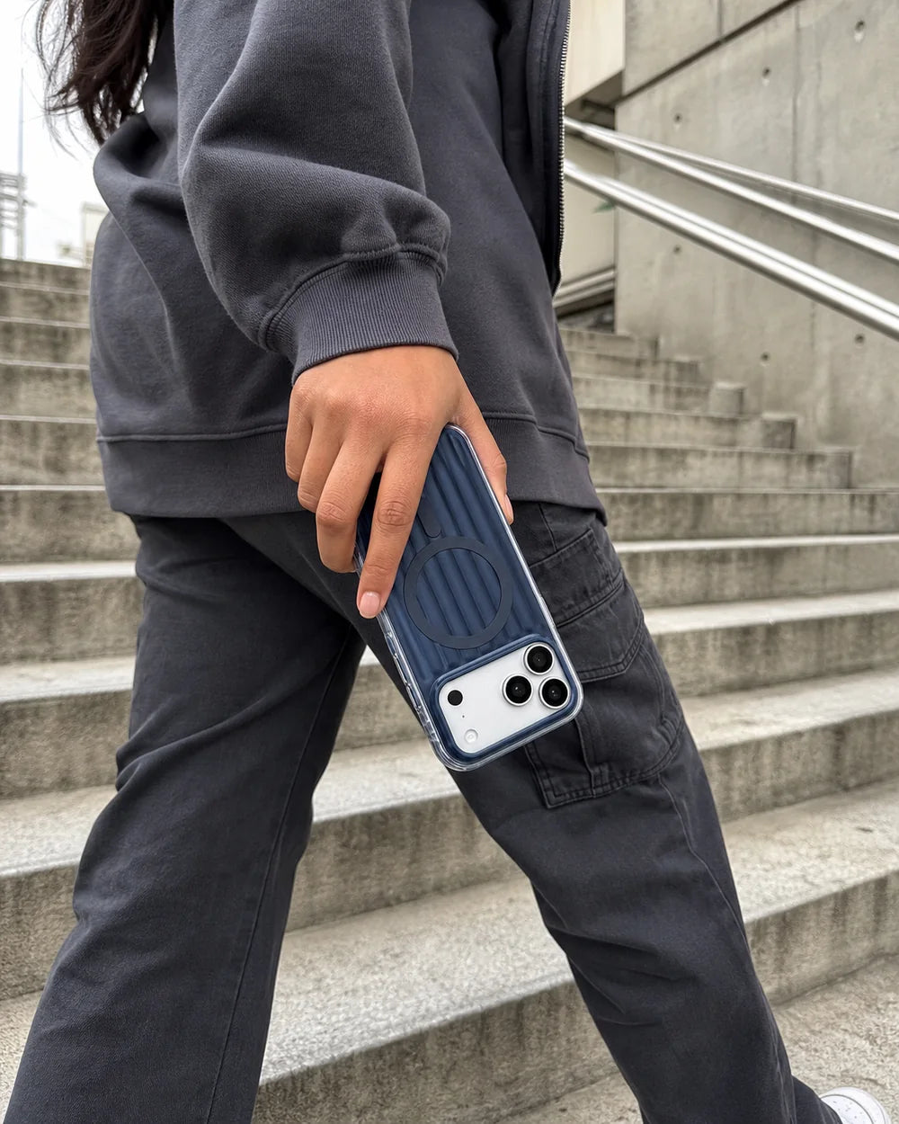 Woman gripping a deep-blue Ribbed CaseBear iPhone 17 Pro Max case while walking on concrete stairs