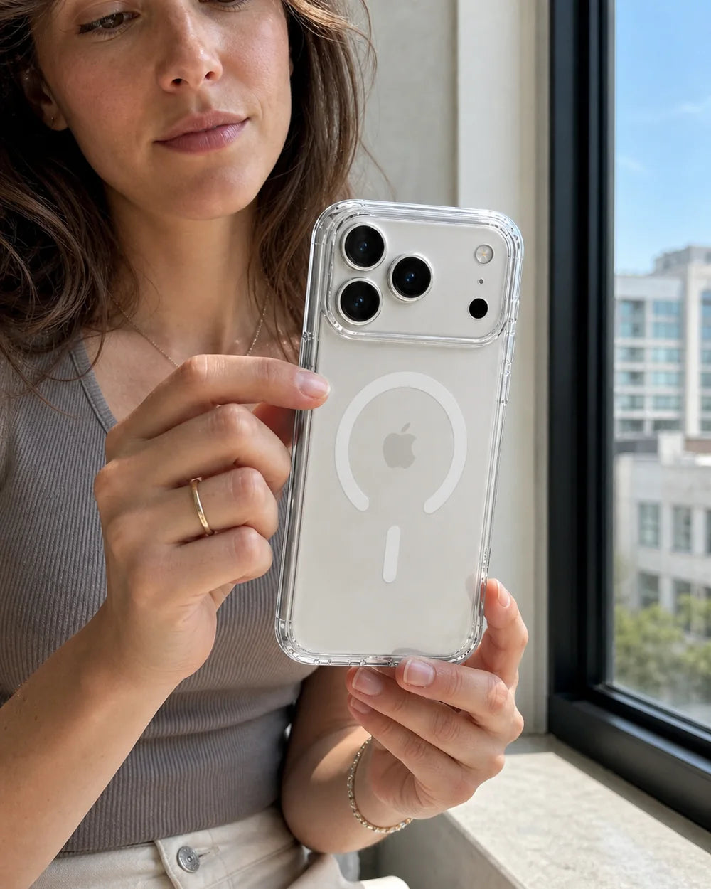 Woman inspecting a clear CaseBear iPhone 17 Pro Max case in direct window light