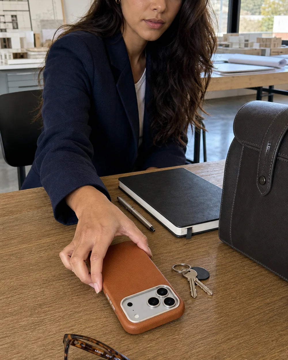 Architect reaching for a classic-brown Leather CaseBear iPhone 17 Pro Max case beside daily work accessories